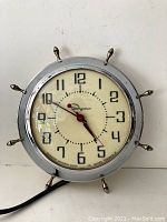 Front view of vintage Ingraham wall clock with chrome ship's wheel frame and visible clock face showing time.