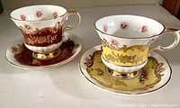 Two vintage bone china tea cups and saucers, one red and one yellow with gold and floral trim detail.