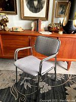 Side and front views of a vintage chrome-framed chair with reupholstered light gray fabric seat and backrest. Chair positioned on patterned carpet with wooden furniture in the background.