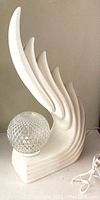 Front and side view of white resin wing-shaped lamp base with glass globe shade resting on base
