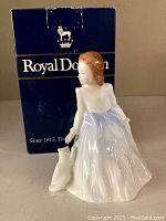 View of the Royal Doulton Andrea figurine showing the woman in a blue and white flowing dress with a small dog beside her and original branded box behind.