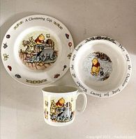 Photo of the vintage Royal Doulton Winnie the Pooh christening set showing a large plate, a small plate, and a mug with character illustrations and text on the rims.