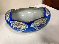 Angled top side view of the blue ceramic dish decorated with white flowers accented in gold.