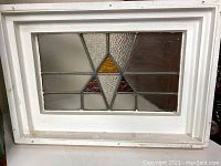 Full view of the rectangular framed stained glass window with white frame and central geometric design.