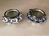 Two Delfts Holland ceramic ashtrays with blue floral patterns, metal rims, and glass inserts, viewed from top and side angles.
