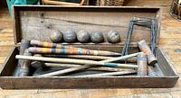 Wooden croquet set components arranged in open wooden box showing mallets, balls, and metal wickets.