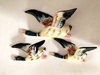 Three vintage hand-painted flying duck wall pockets arranged on a light surface, showing top and side views of each piece.