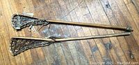 Two vintage wooden lacrosse sticks with netted heads laying on wooden floor, showing condition and details.