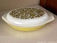 Side view of Pyrex casserole dish showing pale yellow base and white lid with green leaf and berry pattern