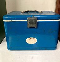 Front view of the blue metal cooler showing latch, white trim, handle, and rust spots.