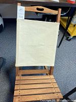 Front view of wood and canvas beach chair showing canvas backrest and wooden slat seat with handle cut-out on top bar.