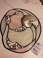 Full view of oval stained glass with blush and cream colored glass, white and translucent beads, and natural shell. Hanging wire included. Small crack visible at bottom edge of bubble glass section.