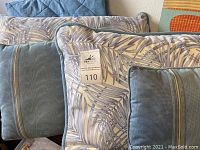 Handmade blue bed coverlet with textured quilting visible behind a group of various blue pillows including patterned and plain king size pillows and smaller accent pillows.