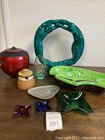 Full view of lot on wooden surface with teal Haeger sculpture, red jar with lid, offset vase, large ashtray, honey jar, tray, and three acrylic dishes