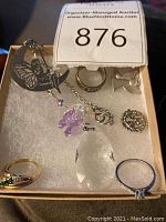 Box showing crystal sun catcher, charms, and rings arranged on white padding