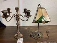 Photo showing the Gorham silver plated multi-arm candelabra alongside the stained glass lily pad lamp on a wooden surface.