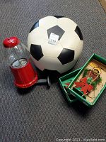 Red gumball machine, soccer ball stool and two boxed Christmas lanterns on grey carpet