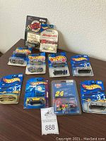 Lot of 10 Hot Wheels collectible cars still in original packaging, displayed on a table against a white wall.
