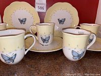 Five Lenox Butterfly Meadow cups and matching salad/dessert plates displayed together, showing scalloped edges and butterfly design.