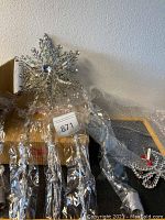 Photo of silver-tone starburst wind chime with dangling bells wrapped in plastic against neutral wall background.