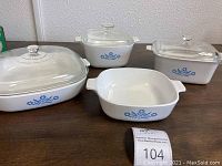 Full view of four vintage Corningware Cornflower casserole dishes with lids on a wooden table.