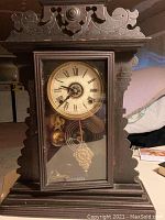 Front view of carved dark wood case, glass front door, dial and pendulum visible