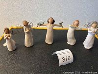 Five Willow Tree figurines arranged side by side, displaying their full figures and wire wings, on a black surface with a catalog number tag.