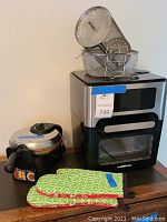 Photo of GoWISEUSA air fryer with multiple metal baskets on top and two green and red patterned oven mitts in front.