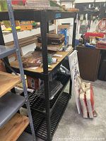 Black plastic shelving unit filled with various items including boxes and bags. Shelving unit has four slatted shelves and is approximately 54 x 35 x 19 inches.
