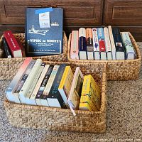 Photo showing three woven baskets holding multiple books including a large hardback titled 'NIPSIC to NIMITZ' and various paperbacks.
