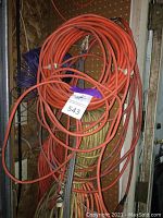 Photo showing multiple orange extension cords hanging on pegboard, with some yellow and purple cords mixed in.