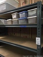 Metal shelving unit with MDF shelves, top shelf holding various plastic storage bins with lids.