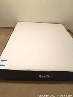 Full view of the queen size memory foam mattress on the floor with a white textured top and black sides.