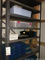 Metal garage shelving unit with multiple storage containers on shelves, mostly blue translucent plastic cases and clear bins.
