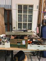Photo showing door with six divided glass window lights, brass deadbolt, and door frame behind a table with boxes of hardware and tapes