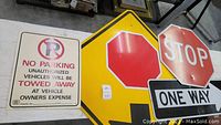 Four street signs laid out on a table showing the Stop Ahead, Stop, One Way, and No Parking signs arranged together.