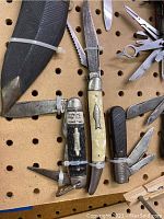 Top-down view showing six folding pocket knives, some with multiple blades extended, including Imperial PROV. R.I. and Swiss Army-style cutters.