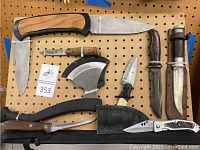 Full view of the assortment of knives and axe on a pegboard, showing variety in size and handle materials, including a Timber Rattler folding knife.