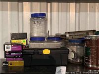Plastic jars on and around a black toolbox, assorted nuts, bolts, screws inside jars, caulking tool visible