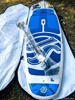 SUP and accessories laid out on grass with board bag open, paddle still in plastic on deck