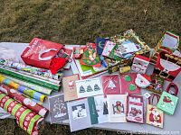Photo showing holiday gift wrapping paper rolls, greeting cards, gift bags, and holiday tags on grass surface.