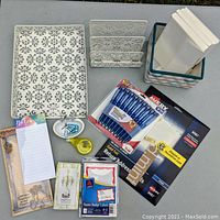 Photo showing punched metal desk tray and mail holder, pack of Avery pens, return address labels, nametag stickers, unopened notepads, cream envelopes in patterned container.