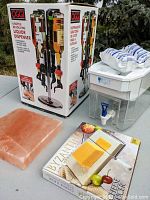 Photo showing OGGI liquor dispenser box, Himalayan salt block, Byzantine cheese board box, Brita pitcher, and replacement filters on table outdoors.