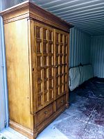 Closed view of a large solid wood armoire with decorative paneled double doors and crown molding, sitting on a wood base with two lower drawers.