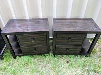 Two dark wood bedside tables placed side by side outdoors on grass, showing overall size, shape, and condition with minor scuffs on surface.