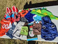 Photo of all items laid on white table showing various pet costumes, sweaters, jackets, and accessories in small and medium sizes.