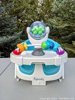 Front view of Ingenuity baby seat with removable tray attached, featuring colorful suction toys and clear dome with green balls inside.