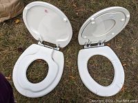 Two white TOPSEAT brand toilet training seats shown outside with lids open and toddler seats pulled down.