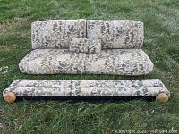 RV couch folded upright with cushions and small pillow, pattern shows beige and brown scroll design fabric, wooden legs visible.
