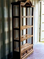 Full view of the tall solid wood shelf with iron bars on sides and back, showing four shelves and decorative curved top.